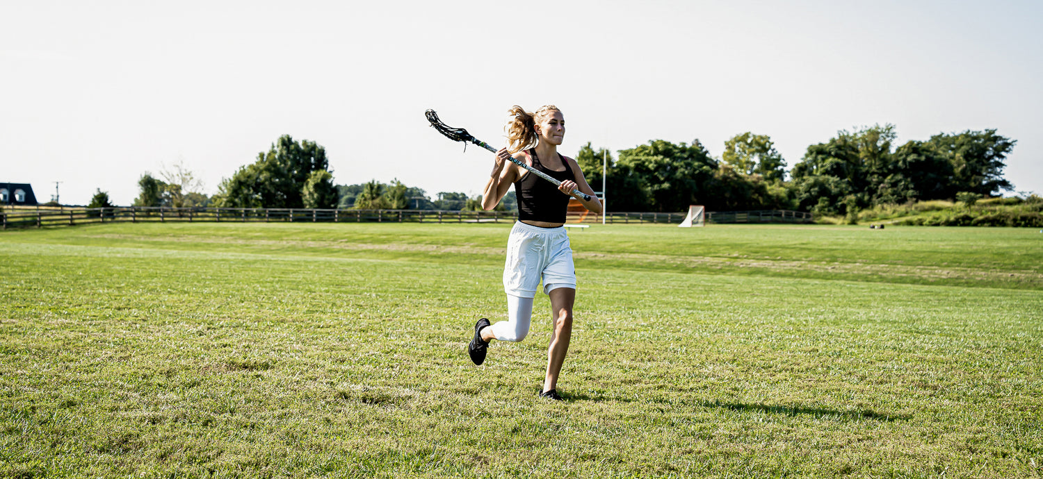 LVLS female athlete wearing white tights running with a lacrosse stick