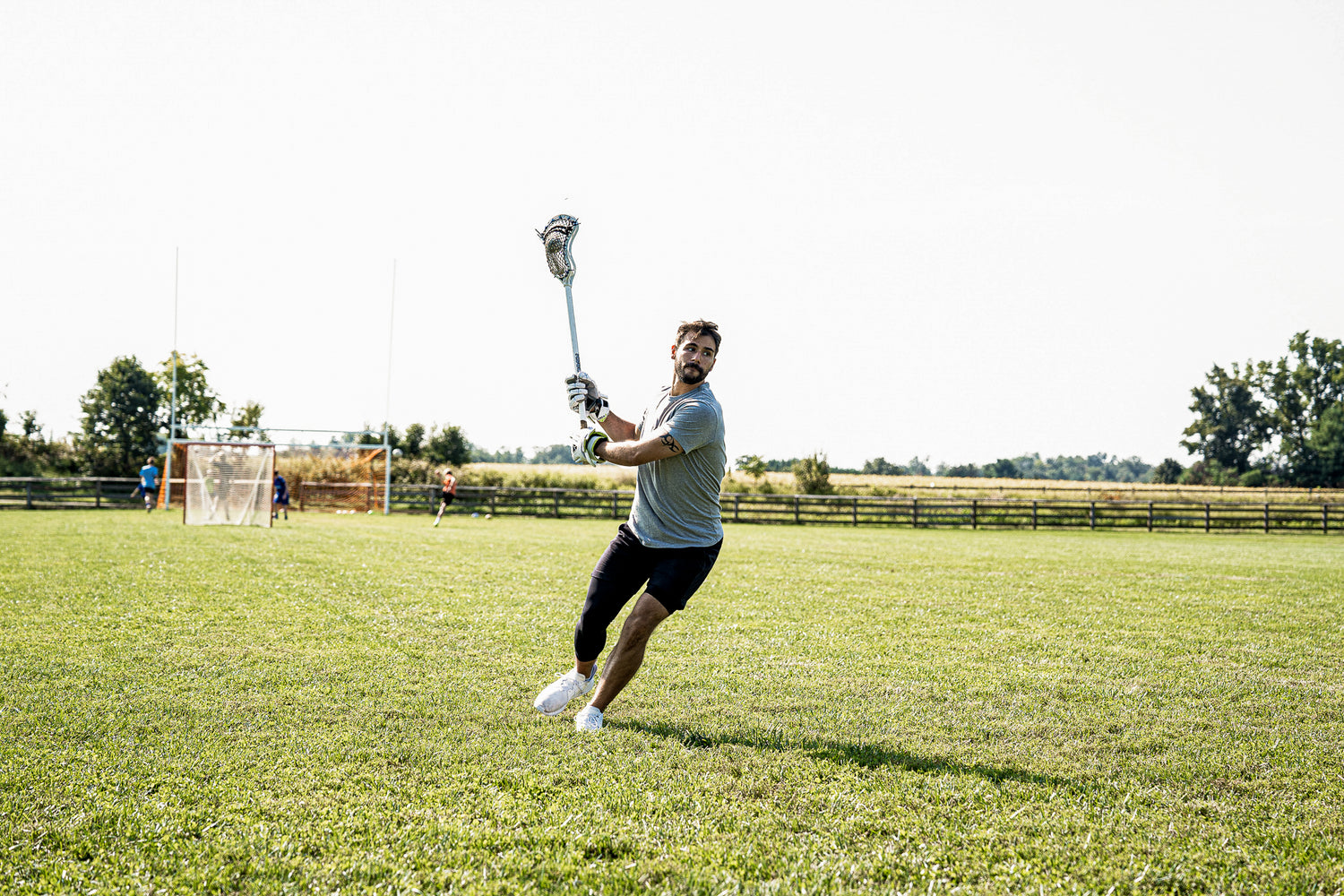 LVLS male athlete wearing black tights standing on a grass hill with a lacrosse stick